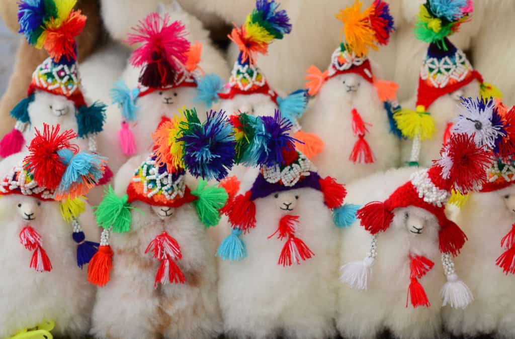 Little toy alpacas with colorful andean hats. All alpacas are lined up in a row and stand three rows behind each other. Soft and fluffy alpacas